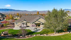 Back of house with a mountain view, stucco siding, a patio, and a yard