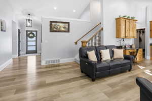 Living room featuring high vaulted ceiling, light wood-style floors, stairs, and recessed lighting