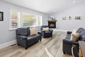 Living room with vaulted ceiling, recessed lighting, light wood finished floors, and a glass covered fireplace