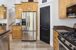 Kitchen with appliances with stainless steel finishes, dark stone countertops, light wood-style flooring, and light brown cabinetry