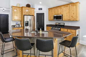 Kitchen with light brown cabinets, light wood-style floors, stainless steel appliances, dark stone countertops, and a kitchen breakfast bar