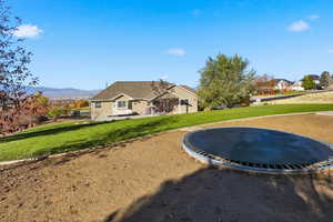 Rear view of house featuring a trampoline, a yard, and a mountain view