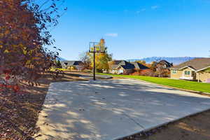 View of sport court with a residential view, basketball hoop, a mountain view, and a yard