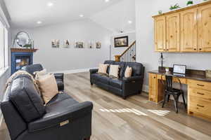 Living room with lofted ceiling, built in study area, light wood-type flooring, a glass covered fireplace, and recessed lighting