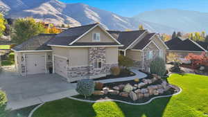 Craftsman house featuring stucco siding, stone siding, an attached garage, a mountain view, and a front lawn