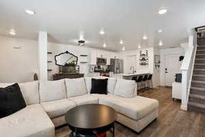 Living room with stairway, dark wood-type flooring, a textured ceiling, and recessed lighting