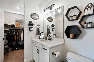 Bathroom with vanity, a walk in closet, light colored carpet, and a textured ceiling