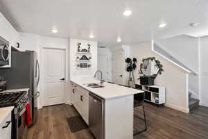Kitchen featuring white cabinets, a peninsula, dark wood-type flooring, a breakfast bar area, and appliances with stainless steel finishes