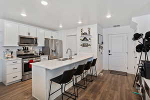 Kitchen featuring stainless steel appliances, white cabinetry, a kitchen breakfast bar, dark wood-type flooring, and a textured ceiling