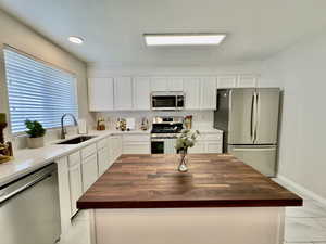 Kitchen with butcher block countertops, stainless steel appliances, white cabinetry, and recessed lighting