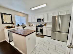 Kitchen with wooden counters, appliances with stainless steel finishes, white cabinets, and a center island