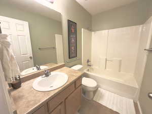 Bathroom featuring vanity,  shower combination, dark tile patterned flooring, and a textured ceiling