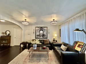 Living room with arched walkways, a chandelier, a textured ceiling, and wood finished floors