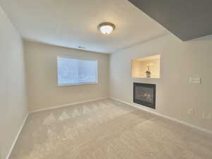 Unfurnished living room with a glass covered fireplace, carpet, and a textured ceiling