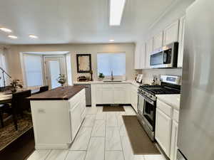 Kitchen with butcher block countertops, white cabinets, stainless steel appliances, light marble finish flooring, and recessed lighting