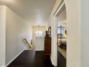Hall with an upstairs landing, dark wood-type flooring, and a chandelier