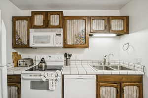 Kitchen with tile counters, white appliances, and brown cabinets