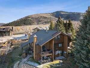 Back of house featuring a deck with mountain view, a chimney, stairway, a view of trees, and a shingled roof