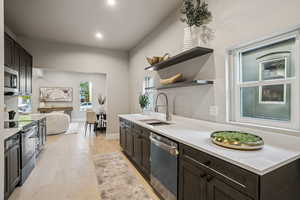 Kitchen featuring open shelves, dark brown cabinetry, light wood finished floors, stainless steel appliances, and light stone counters
