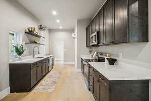 Kitchen featuring dark brown cabinetry, stainless steel appliances, open shelves, light wood-type flooring, and recessed lighting