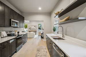 Kitchen featuring open shelves, light wood finished floors, stainless steel appliances, and light stone countertops
