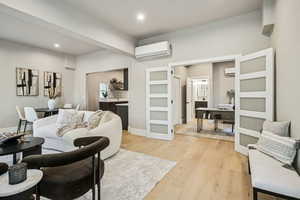 Living area featuring light wood-style floors, a wall mounted AC, and recessed lighting