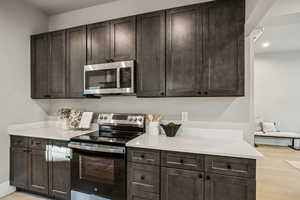 Kitchen with stainless steel appliances, dark brown cabinets, light stone counters, and light wood finished floors