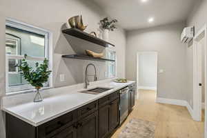 Kitchen featuring open shelves, dark brown cabinets, light wood finished floors, stainless steel dishwasher, and light stone countertops