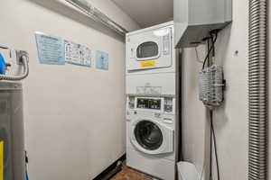 Laundry room featuring stacked washer / drying machine, water heater, and electric water heater