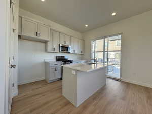Kitchen featuring recessed lighting, stainless steel appliances, an island with sink, light wood-type flooring, and light stone counters