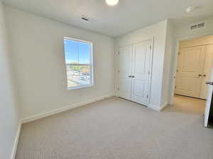Unfurnished bedroom with a textured ceiling, light carpet, and a closet