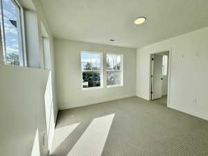 Carpeted empty room with a textured ceiling and baseboards