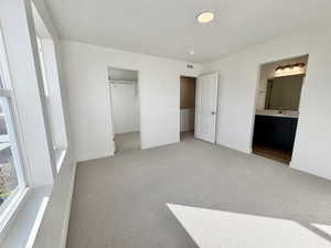 Unfurnished bedroom featuring a spacious closet, light carpet, a textured ceiling, and ensuite bathroom