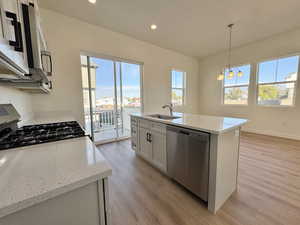 Kitchen featuring a center island with sink, decorative light fixtures, appliances with stainless steel finishes, light stone countertops, and recessed lighting