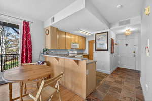 Kitchen with a peninsula, a breakfast bar area, white appliances, dark stone finish flooring, and light countertops