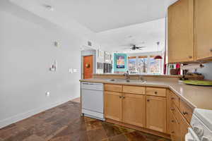 Kitchen featuring stone tile flooring, a peninsula, white appliances, light countertops, and light brown cabinetry