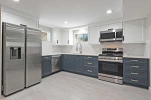 Kitchen with white cabinets, stainless steel appliances, tasteful backsplash, blue cabinetry, and recessed lighting