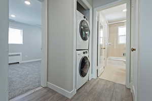Laundry area with estacked washer and dryer, radiator heating unit, light wood-type flooring, and recessed lighting