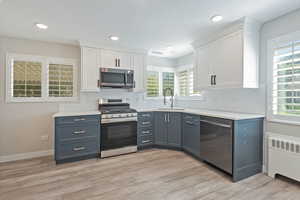 Kitchen featuring white cabinets, appliances with stainless steel finishes, radiator heating unit, recessed lighting, and light wood-style floors