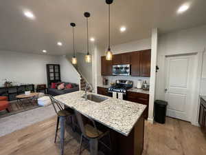 Kitchen featuring a kitchen bar, dark brown cabinets, a center island with sink, stainless steel appliances, and light wood-style floors