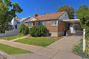 View of front of home with brick siding, driveway, an attached carport, and a chimney