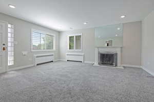 Unfurnished living room featuring radiator heating unit, recessed lighting, light carpet, and a fireplace with flush hearth