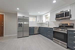 Kitchen with stainless steel appliances, white cabinetry, decorative backsplash, recessed lighting, and light stone counters