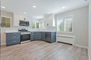 Kitchen featuring white cabinets, radiator, appliances with stainless steel finishes, recessed lighting, and light wood-type flooring