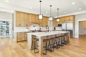 Kitchen featuring light brown cabinets, a breakfast bar, built in appliances, and recessed lighting