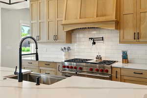 Kitchen with light brown cabinets, double oven range, premium range hood, light stone counters, and decorative backsplash