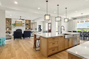 Kitchen featuring open floor plan, a kitchen bar, a fireplace, decorative light fixtures, and light stone counters