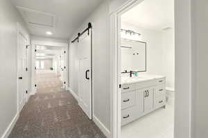 Corridor with light carpet, a barn door, light tile patterned flooring, recessed lighting, and attic access