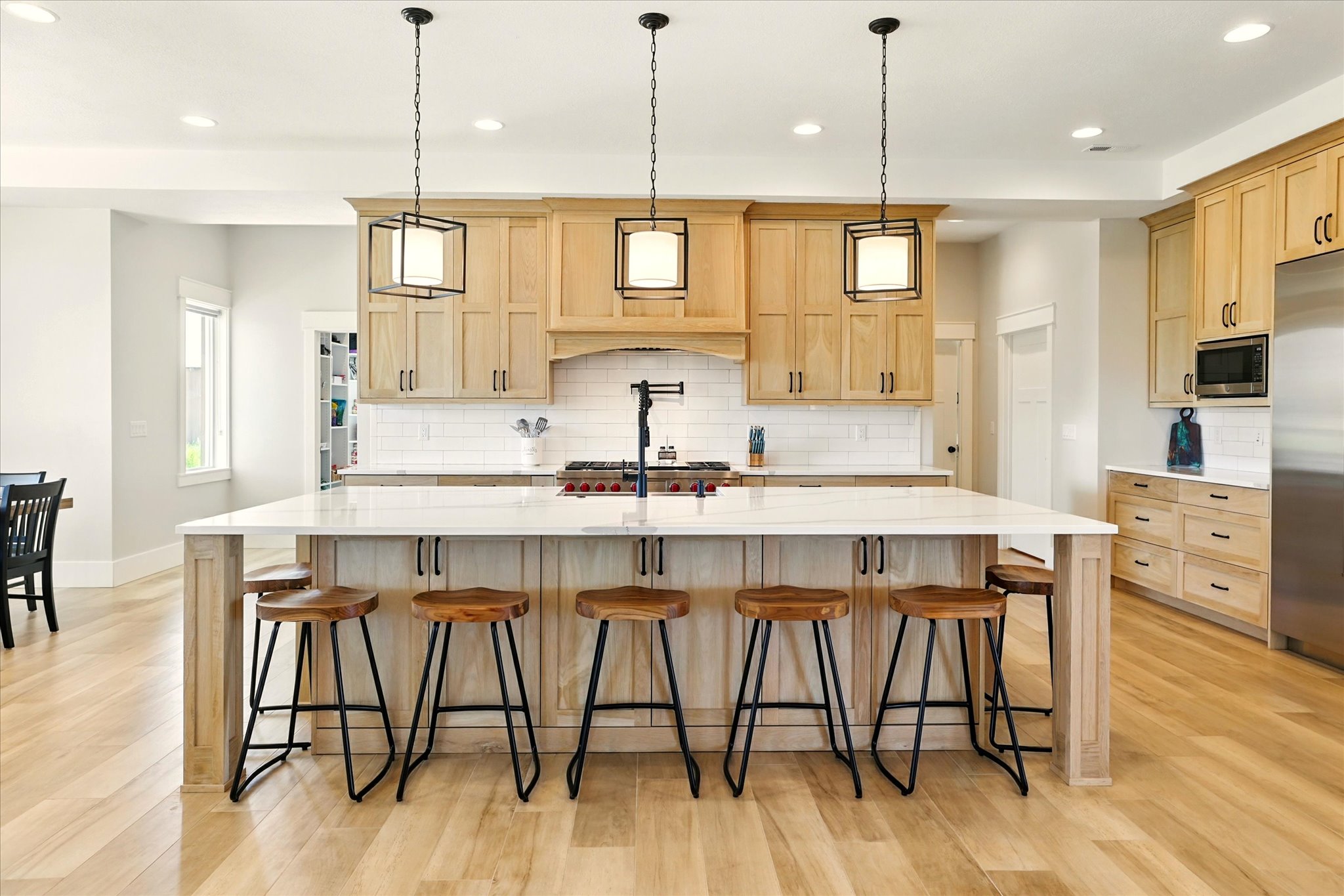 Kitchen with light brown cabinets, a large island with sink, decorative backsplash, recessed lighting, and light wood-type flooring