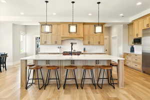 Kitchen with light brown cabinets, a large island with sink, decorative backsplash, recessed lighting, and light wood-type flooring